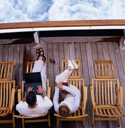 Overhead view of a man and woman sitting on a boat deck at sea, using marine internet on a laptop.